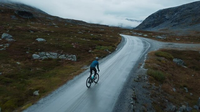 Young solo cyclist man, male rides on high elevation mountain in cold Norway. Adventure at Scandinavian nordic destination. Cycle bike touring life trend. Challenge travel lifestyle concept.