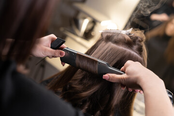 close-up of the hands of the master in the spa salon straighten the hair with an iron in the spa...
