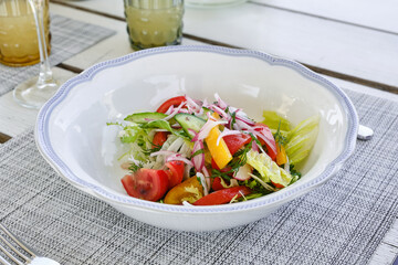 Vegetable salad with cucumbers, tomatoes, onions and peppers in a white plate in a restaurant. Shallow depth of field