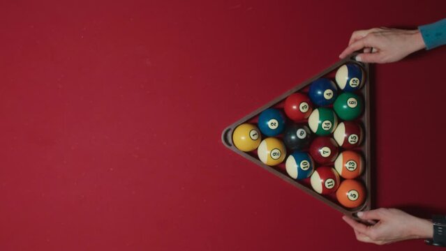 Young female hands picking up triangle pyramid form before billiard pool game of 15 balls beginning on red table. Hobby, professional game, sport. 15 colorful balls breaks on top view shot, 4k footage