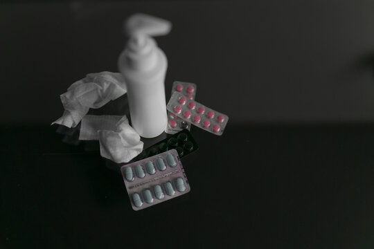 Red and blue blisters with tablets on a dark background, used napkins and white medical vessel. High quality photo