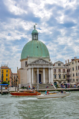 In foreground a sleek Water Taxi passes a vaporetto on the Grand Canal before the 18th century San Simeone Piccolo Church (also called San Simeone e Giuda) with a temple-front modeled on the Pantheon.