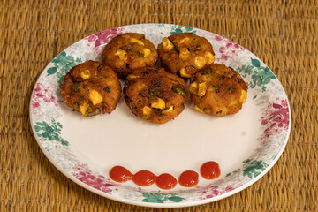 Tasty deep-fried corn and vegetable cutlets are served on a white plate with red tomato sauce.