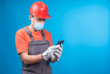 Male builder in face mask browsing social media on smartphone
