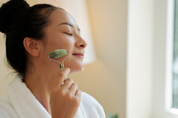 Young Asian woman enjoying massage with jade face roller in the morning © DragonImages