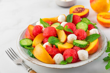 Fruit summer salad made of fresh fruits, mozzarella cheese, cucumbers and mint on white table. Healthy food