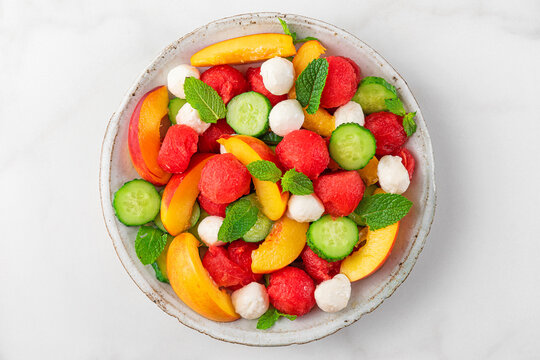 Healthy summer fruit salad with mozzarella cheese in a plate on white marble background. top view