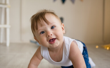 portrait of a baby boy with a squint crawling on the floor in the nursery - obrazy, fototapety, plakaty