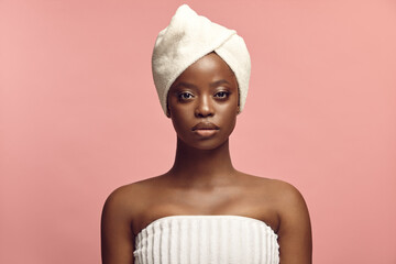 Headshot front portrait of beautiful black skin woman in spa towel on a pink background with a free...