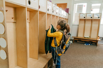 Little girl with backpack hanging her jacket at school