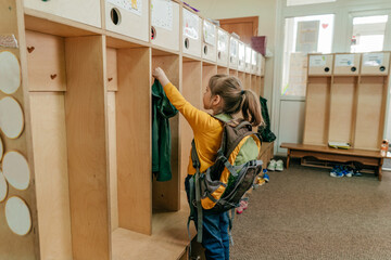 Little girl with backpack hanging her jacket at school