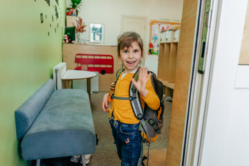 Happy little girl with backpack standing near the door at school