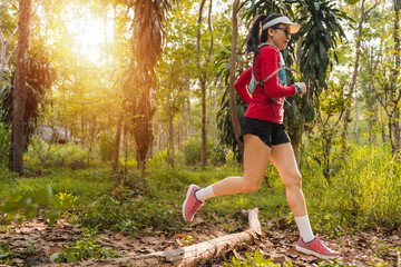 Young fitness sportswoman trail runner running in the tropical forest park in the evening