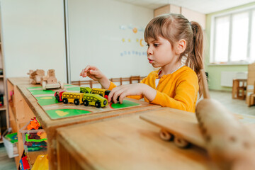 Little girl playing with wooden train on the table at kindergarten