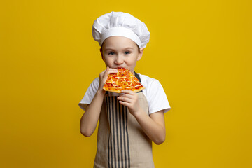 A little funny boy cook of 6-7 years old in a hat and apron holds a rolling pin in his hand for dough and points it aside on a yellow studio background in a black circle. Concept