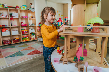 Little girl playing with wooden house at kindergarten