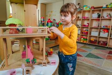 Little girl playing with wooden house at kindergarten