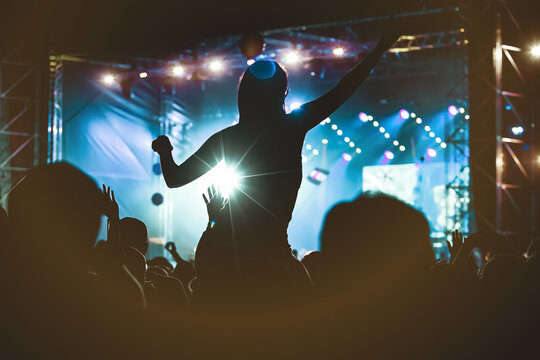 Girl silhouette with raising hands and mobile phone during enjoying music concert.