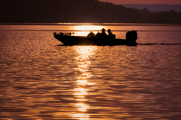 Bass fishermen in a bass boat on the lake, early morning sunrise.