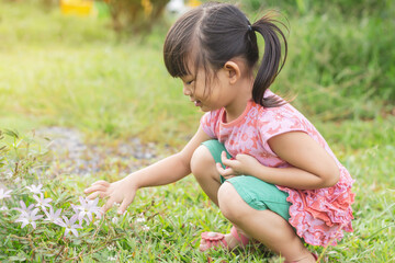 Portrait​ image​ of​ 4-5​ years​ old​ baby.​ Happy​ Asian child girl picking and touching the flowers and​ grass​ at the garden field. Learning​ and​ development​ of​ kid​ concept.