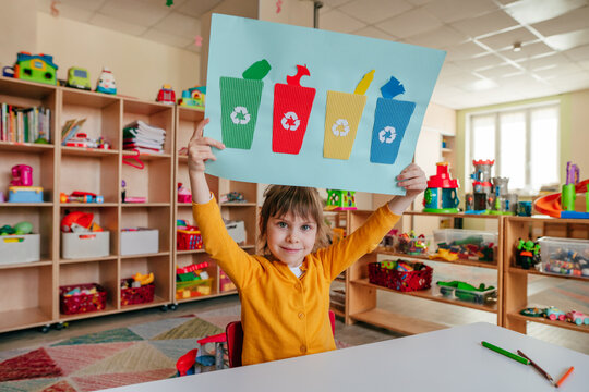 Little girl holding poster of garbage containers for sorting at kindergarten