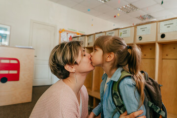 Mother kissing her daughter standing near the wardrobe at school
