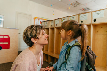 Mother kissing her daughter standing near the wardrobe at school