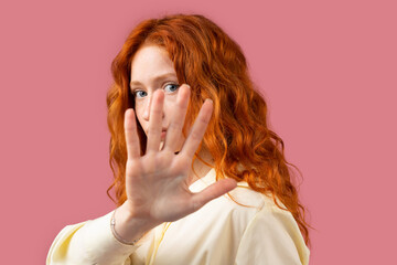 Close up photo of a bright redhead woman showing stop sign with her palm posing on a pink...