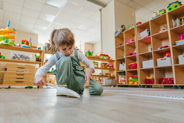 Little girl sweeping the floor using a dustpan and a broom at kindergarten