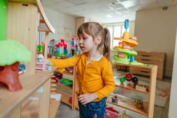 Little girl playing with wooden house at kindergarten