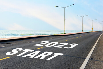 Fototapeta premium Start new year 2023 on asphalt road with marking line for given direction and sea landscape. Road to recovery concept and business success idea