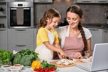 A child cook and her mother prepares healthy food according to a recipe from the Internet