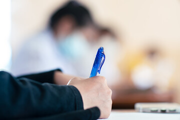 Student taking exam while wearing face mask due to coronavirus emergency. Young woman sitting in...