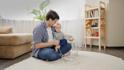 Young caring father teaching his baby son not to touch electric plugs, wires and cables at home.