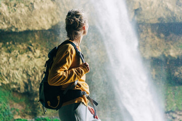 Woman hiker with a backpack in a mountain canyon near a large waterfall. - obrazy, fototapety, plakaty