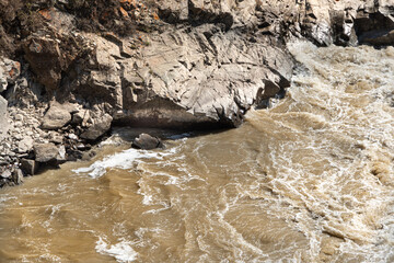 Muddy stream in mountain canyon. Yellow dirty river after flooding in early spring. Dry sheer cliffs form riverbed