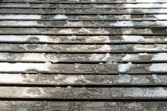 Wooden planks of bridge with ice as background. Trail froze after snowfall, danger to pedestrians.