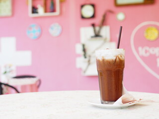 Ice coffee in a tall glass with cream poured over and coffee beans.