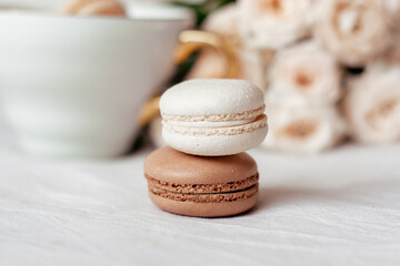 Sweet dessert, vanilla and chocolate macaroons on white roses background, romantic morning breakfast at bed