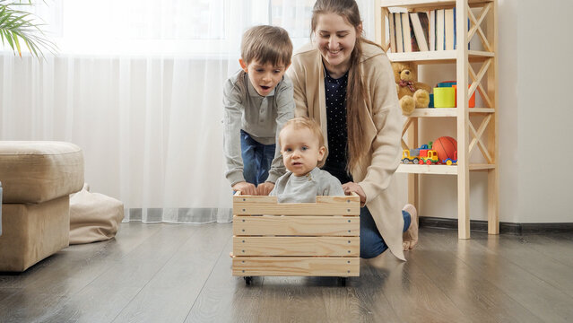 Cute baby boy sitting in wooden toy box while his family riding him at living room.