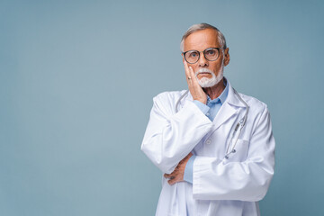 Bearded senior doctor in black-rimmed glasses with stethoscope props up cheek with hand pityingly....