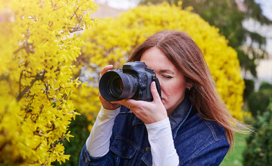 Female photographer take photo outdoors on flower street landscape holding a camera, woman hold digital camera in her hands. Travel nature photography, space for text.