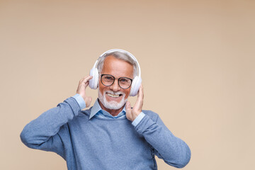 Happy senior man listens to dynamic music in headphones. Cheerful elderly person in glasses has fun...