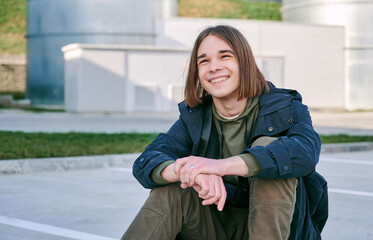 Closeup portrait of laughing teenager boy sitting on skateboard outdoor during summer activities.