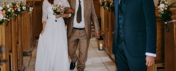 Young bride with her father walking towards the groom in a church