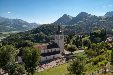A church with a tall tower, a small cemetery and meadows surrounded by mountains in summer in Gruyeres, Switzerland.
