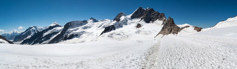 Fototapeta na wymiar Glacier covered with a layer of snow in summer in Switzerland. High rocky mountains, a path in the snow for alpine hiking.