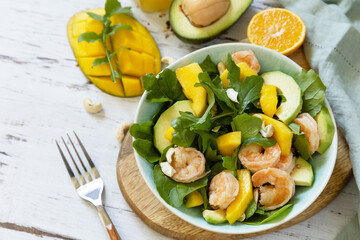 Vegetarian vegan healthy food. Salad with arugula, mango, avocado, shrimp, pecans and dressing of olive oil, honey and wine vinegar on a white rustic kitchen table.