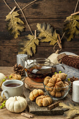 Autumn tea concept. Cookies with pumpkin puree, black tea in a glass teapot, fall decor