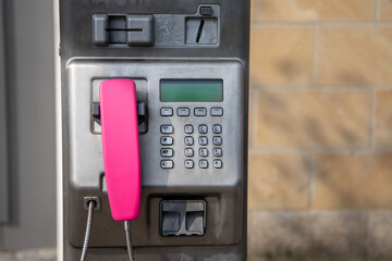 An old telephone machine with a pink handset. Street phone.